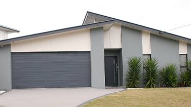House with blue exterior, double garage, and manicured lawns.